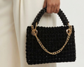 Black beaded handbag with gold chain held by a person wearing a white outfit.