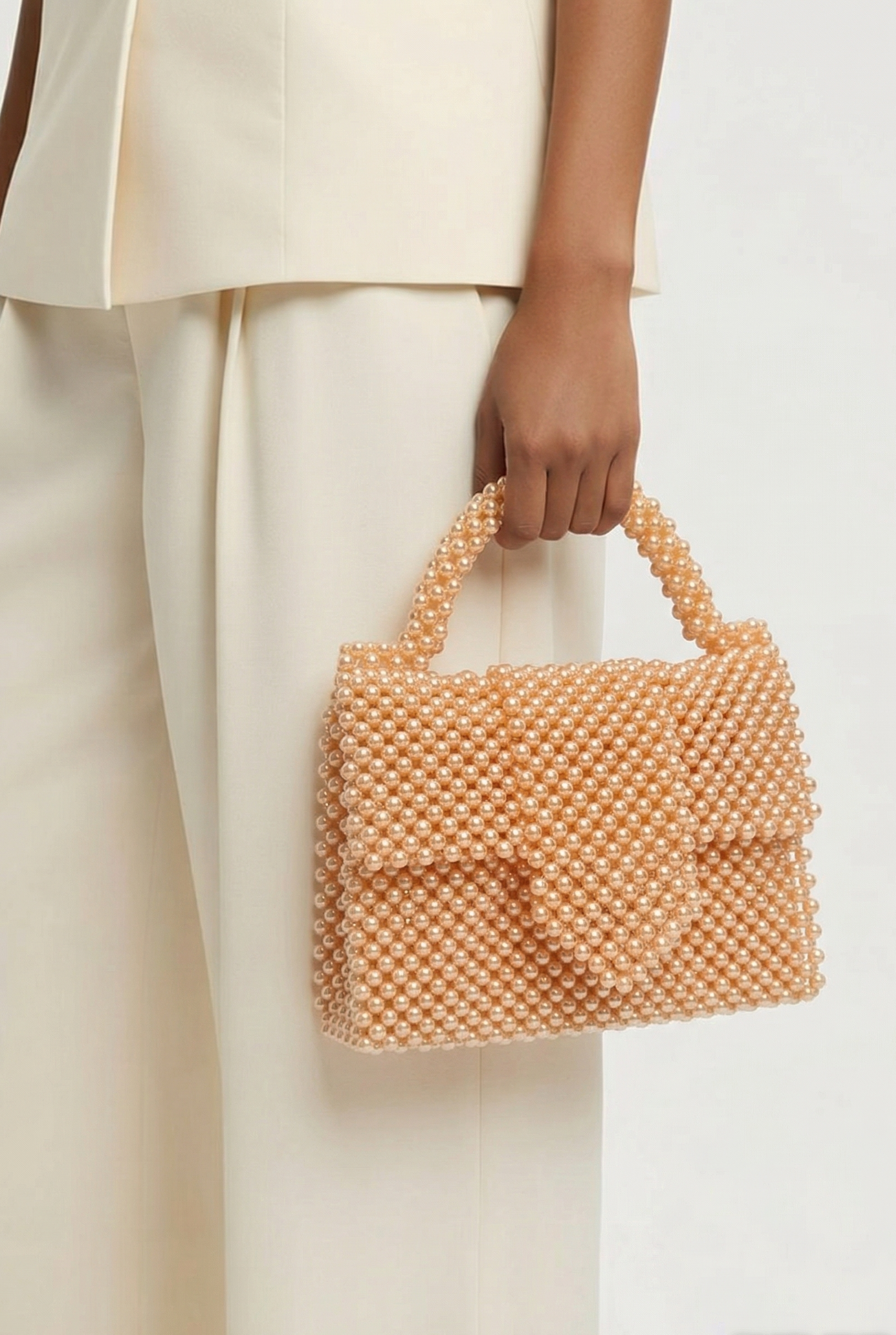 Person holding a peach-colored beaded handbag against a neutral background