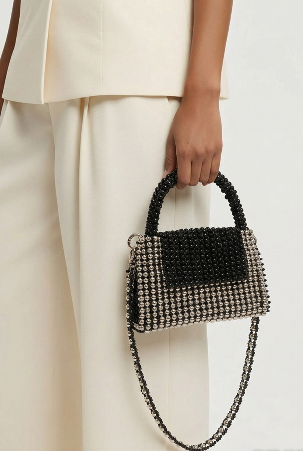 Person holding a black beaded handbag against a white background
